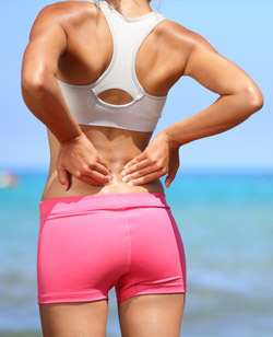 Back pain. Athletic woman in pink sportswear standing at the sea